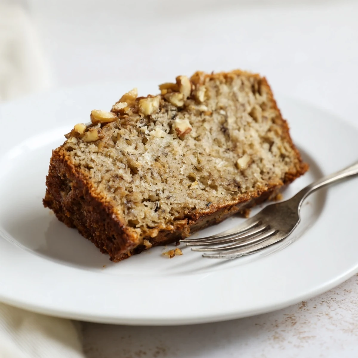 Slice of moist delicious banana bread showing soft interior crumb served on white plate with napkin