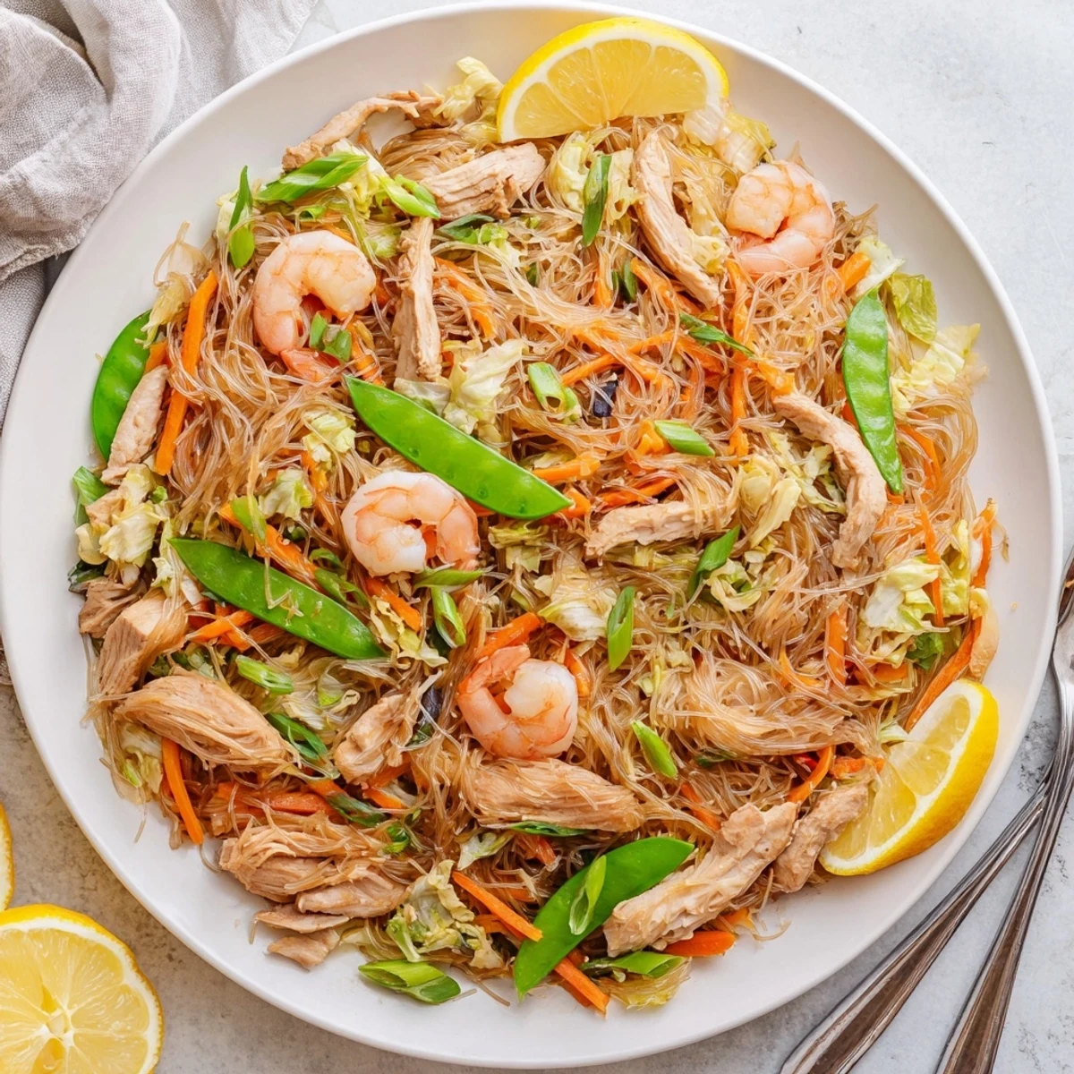 Golden traditional Pancit Bihon stir-fry loaded with tender chicken, shrimp, and colorful vegetables in a savory soy-based sauce
