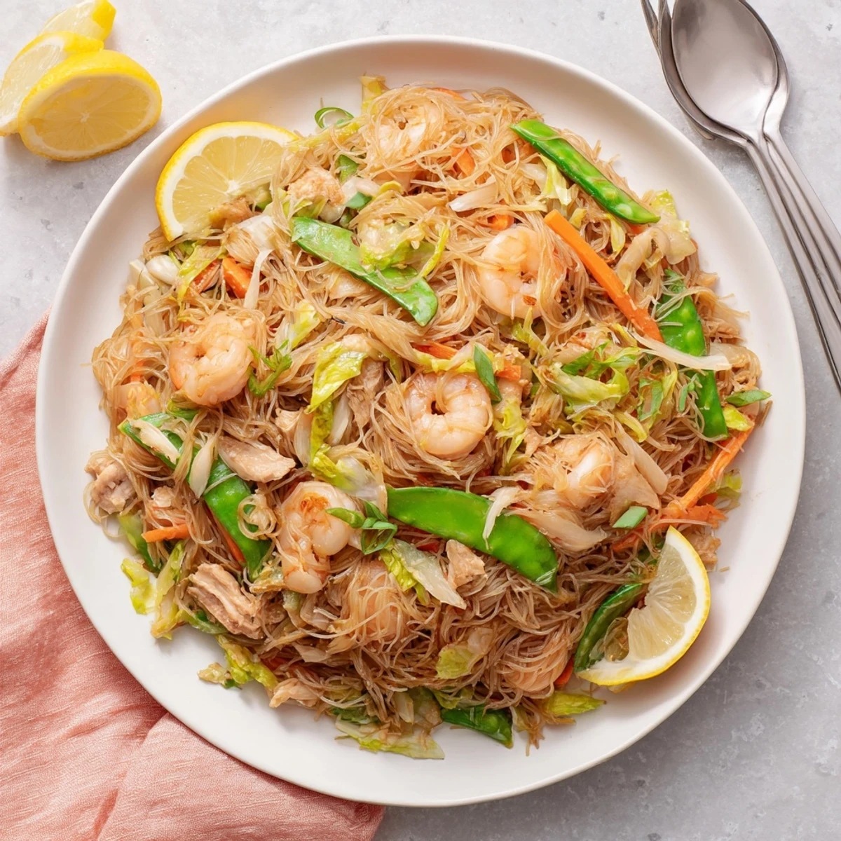 Authentic traditional Pancit Bihon noodle dish garnished with fresh scallions and served with bright lemon wedges for squeezing