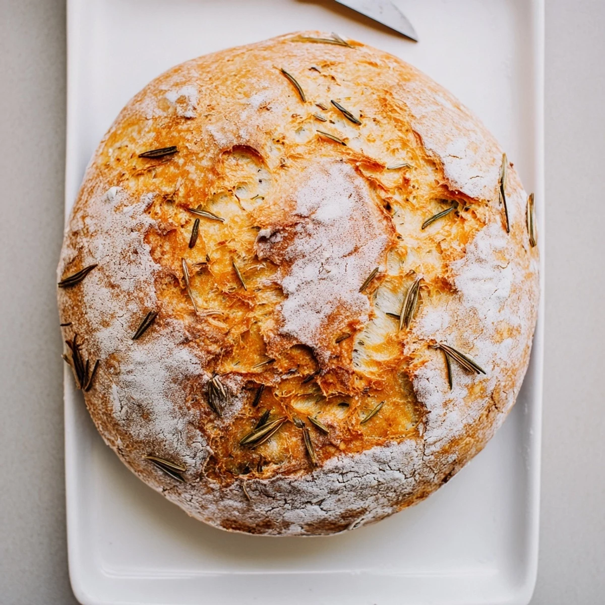 Rustic round bread baked in Dutch oven with rosemary sprigs and minced garlic