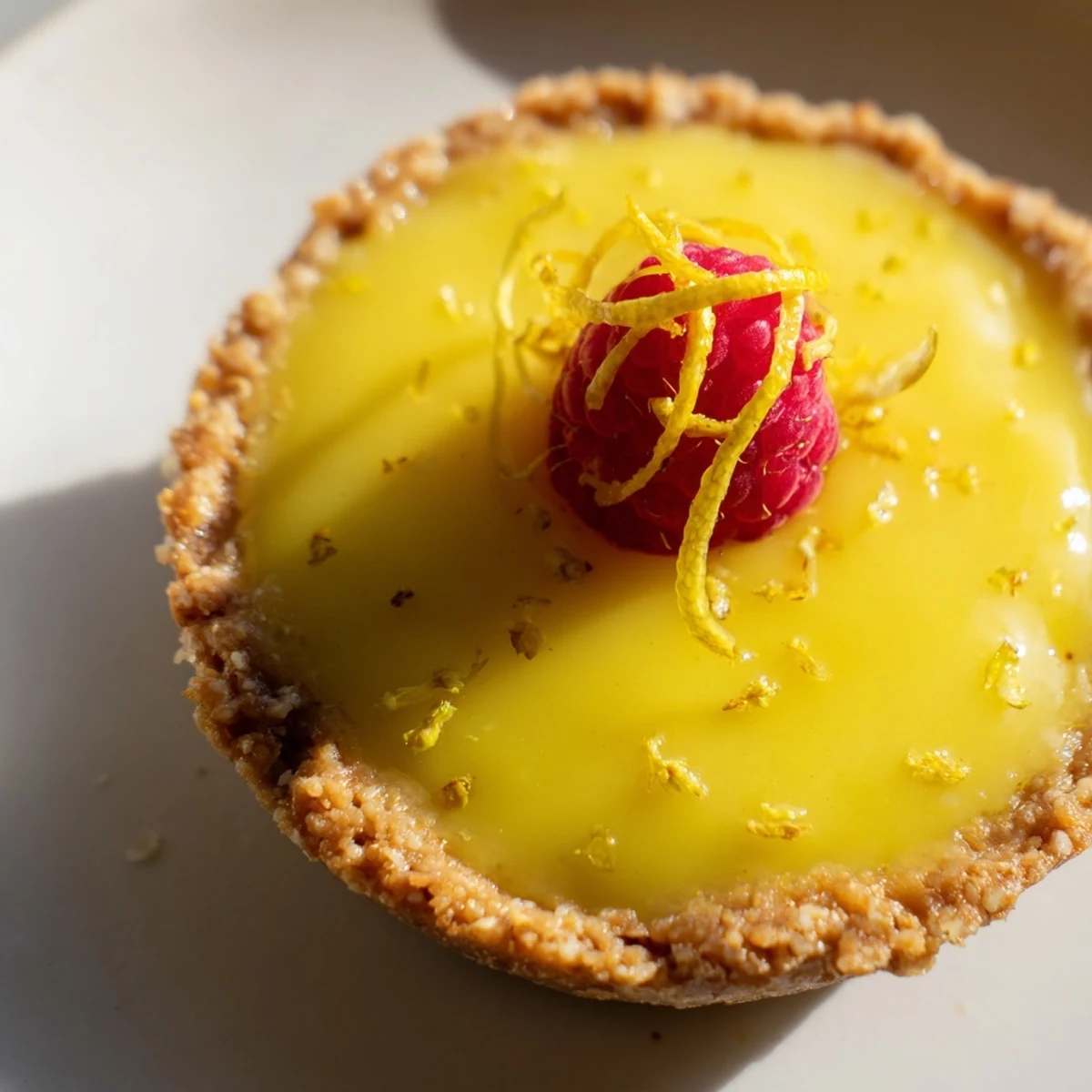 Creamy mini vegan lemon tarts garnished with lemon zest and edible flowers on white serving platter