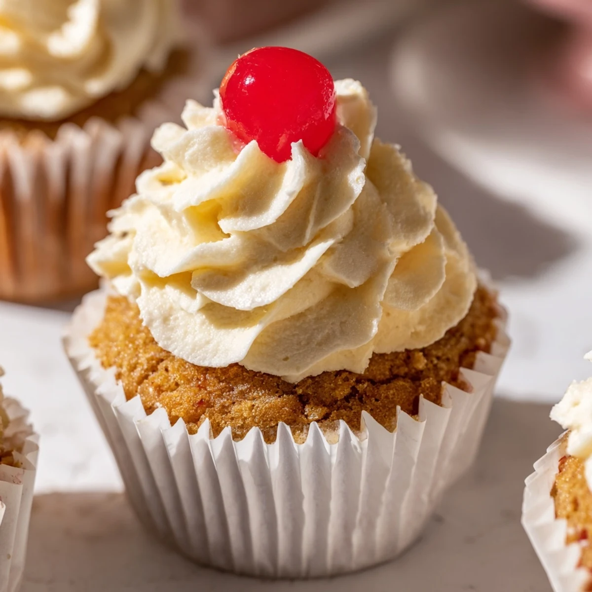 Moist banana milkshake cupcakes topped with fluffy vanilla frosting and bright red maraschino cherry garnish