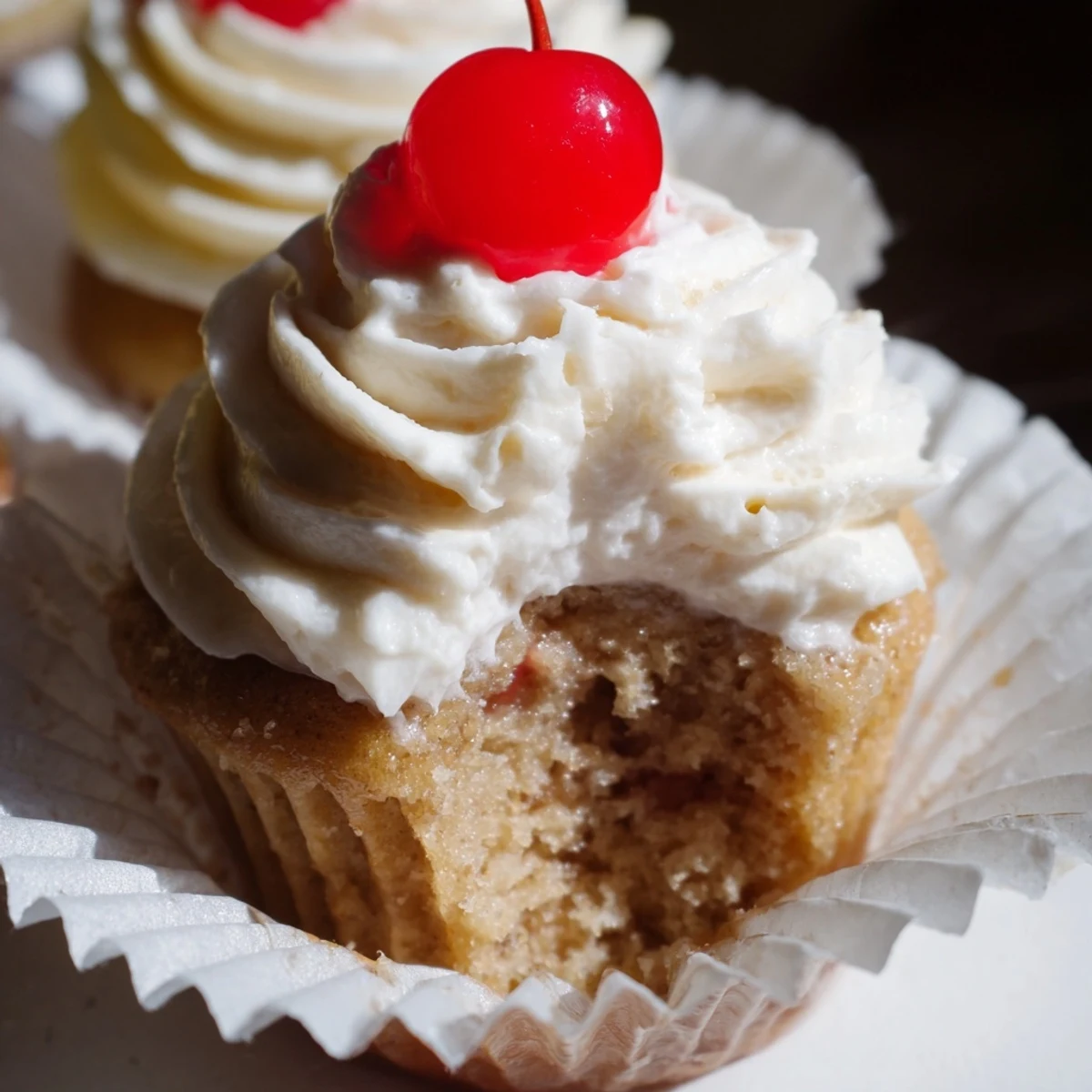 Golden banana milkshake cupcakes with creamy swirled frosting served on rustic white ceramic plate