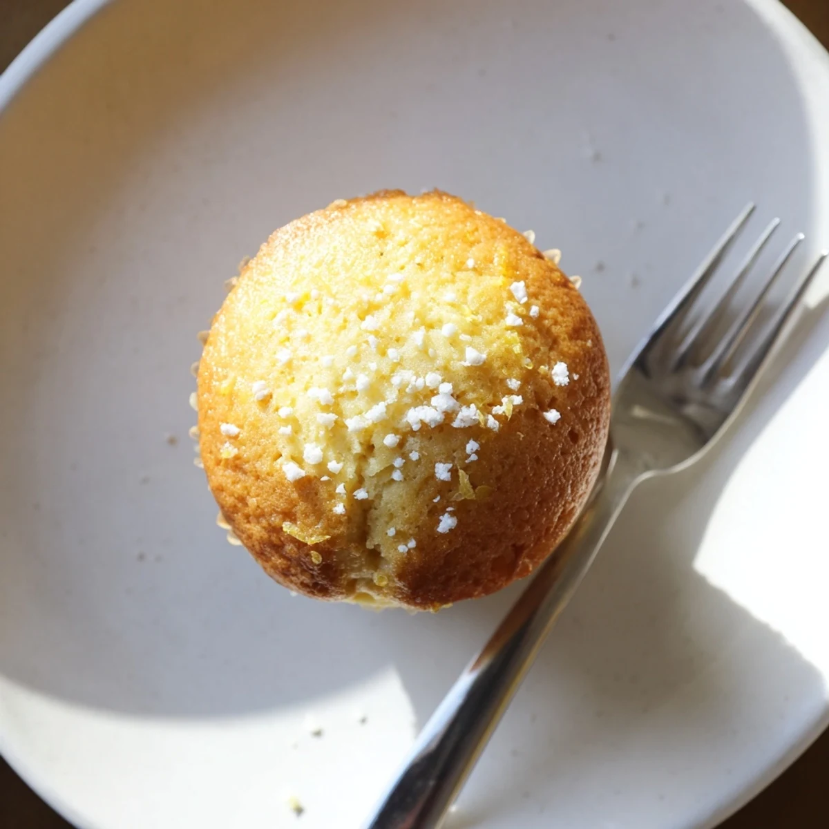 Moist lemon cream cheese muffins cooling in lined muffin tin with golden domed tops