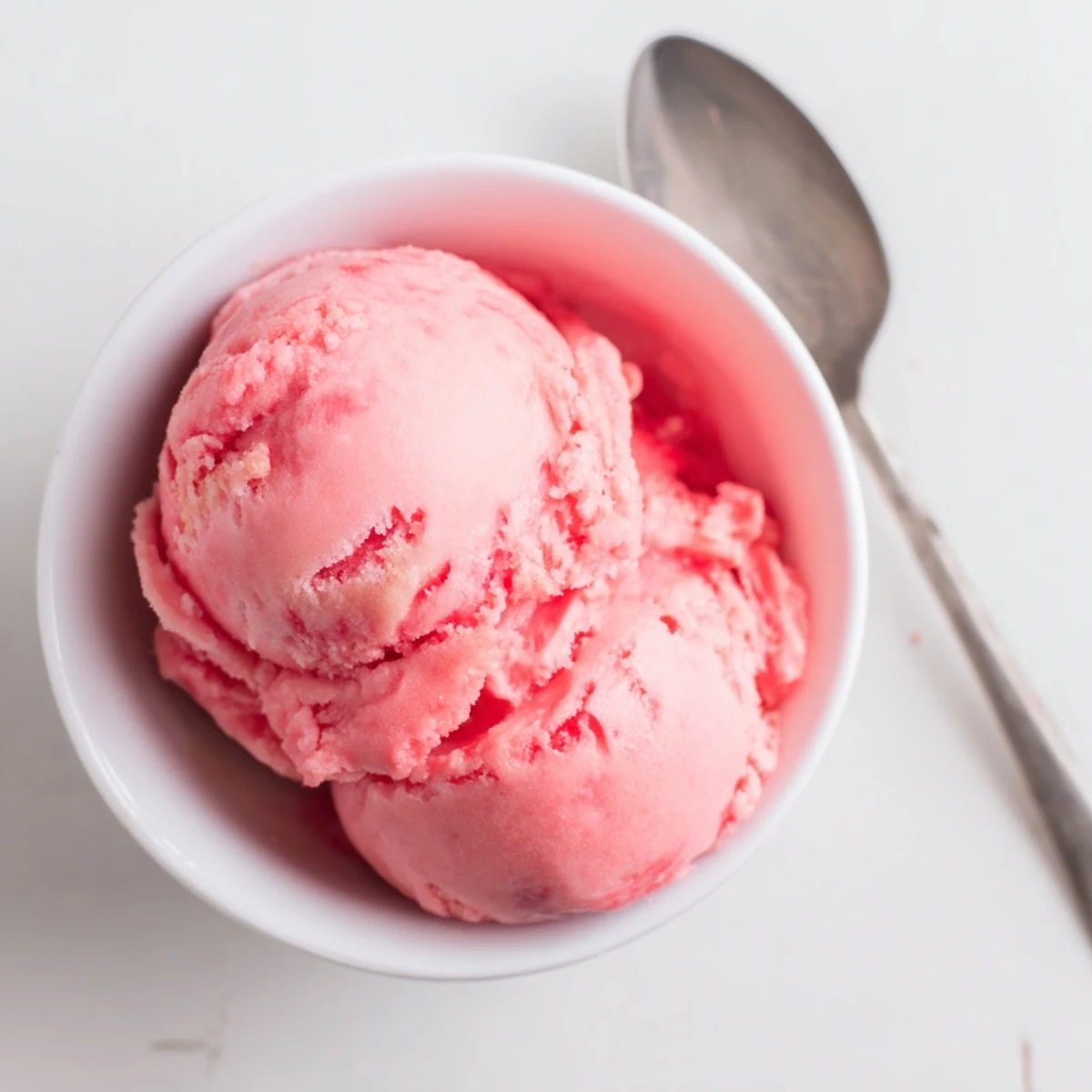 Pink scoops of creamy watermelon ice crystals garnished with fresh mint leaves on a chilled dessert bowl