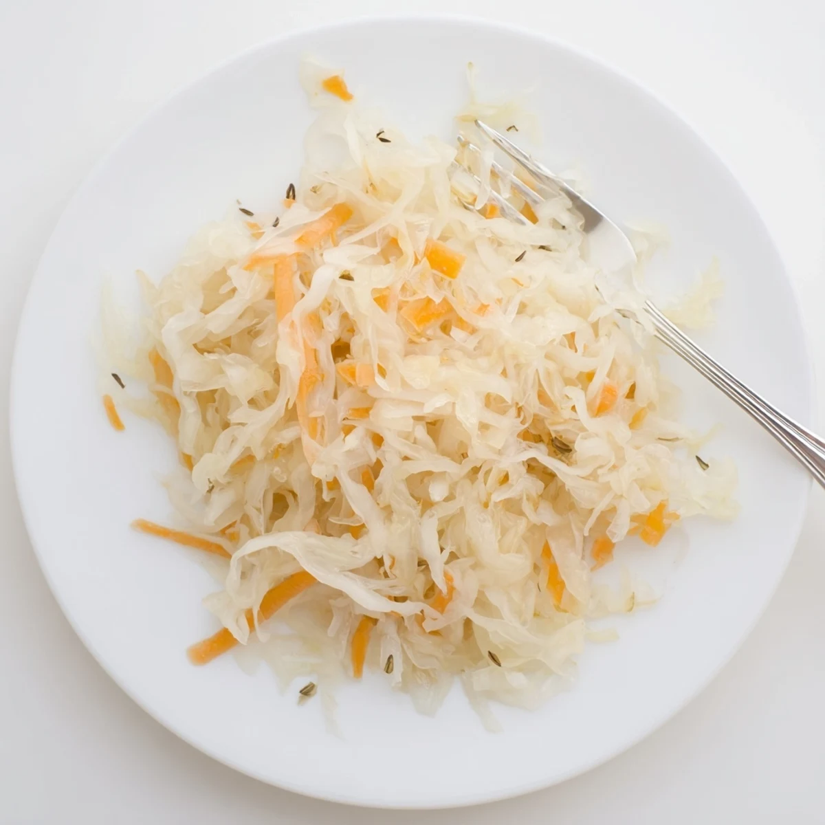 Naturally fermented sauerkraut mounded in white bowl alongside caraway seeds and crisp shredded cabbage