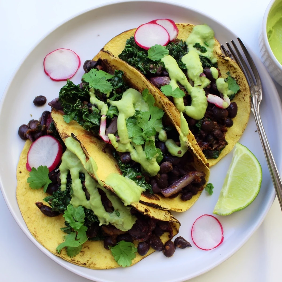 Smoky black bean kale tacos drizzled with vibrant green sauce on warm tortillas