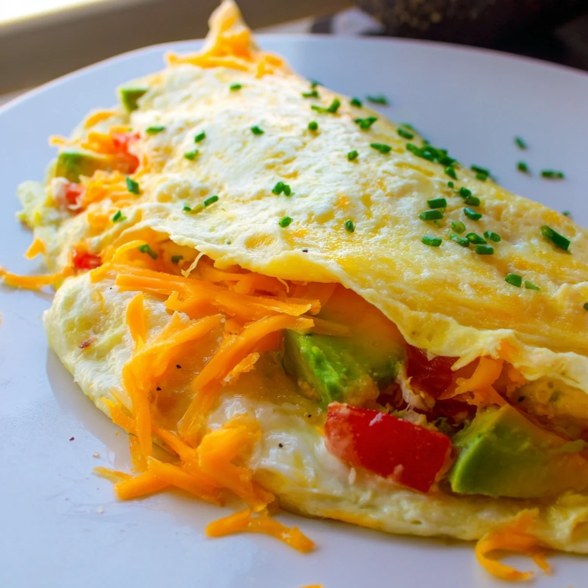 Creamy avocado cheesy tomato omelette served on a white plate with fresh chives
