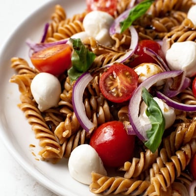 Close-up of Caprese Pasta Salad drizzled with balsamic vinegar in a white ceramic bowl